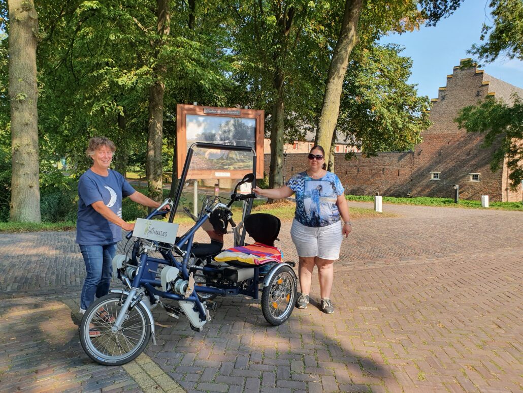Carla en Marijke naast de duofiets en voor het laatste schilderij van de schildersroute.